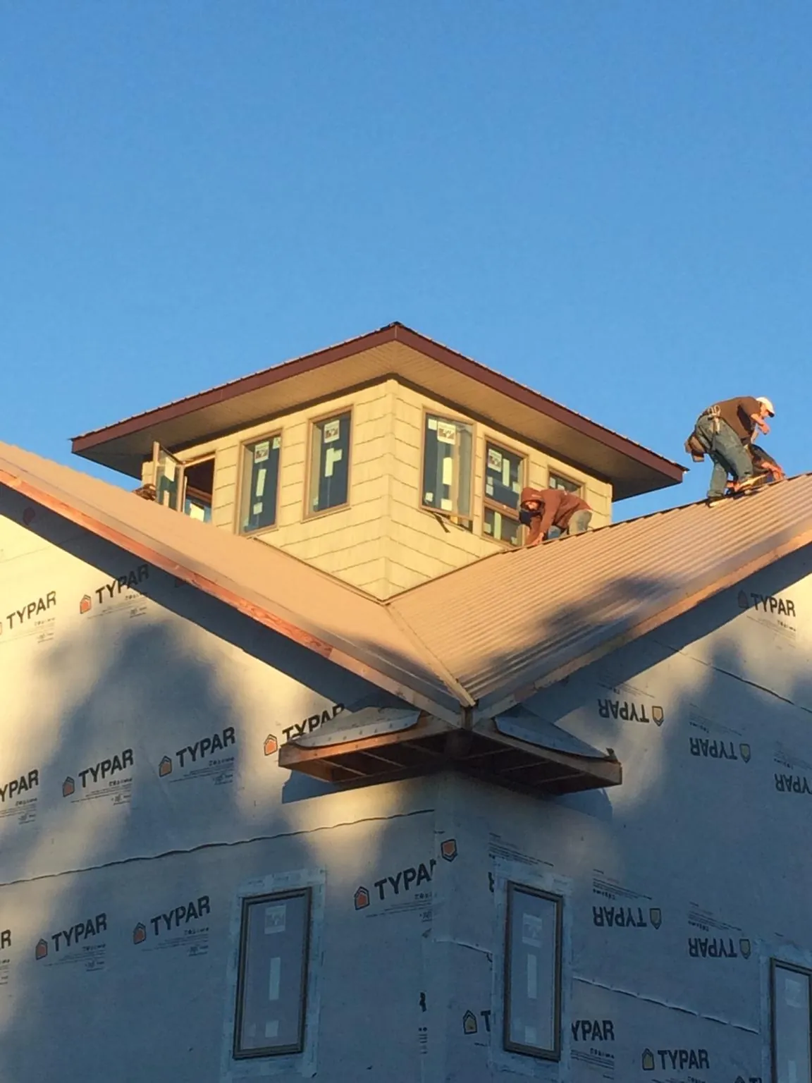 Roofers working around a rooftop cupola on a new metal roof at sunset in Homestead